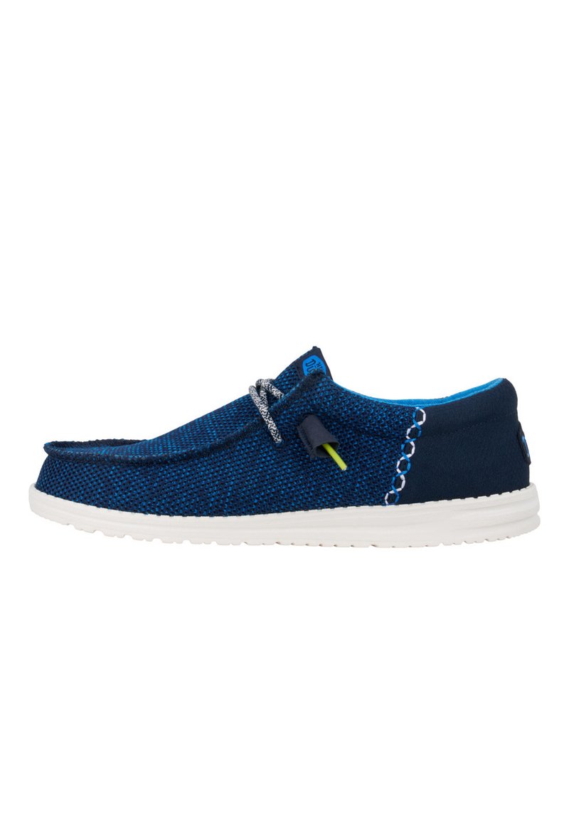 Zapato navy azul sin cordones con parte superior de tejido texturizado, suela de goma blanca, costura decorativa y cordones grises con un detalle de color de acento.