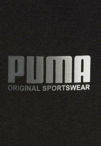 Tessuto nero con un grande logo metallico argento "PUMA" e il testo "ORIGINAL SPORTSWEAR" in un font moderno e audace.