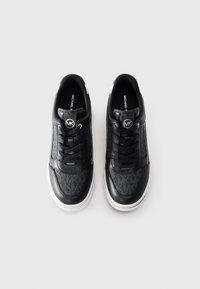 Ein Paar schwarze und graue Michael Kors Sneaker mit weißen Sohlen, Schnürdesign und MK-Logo auf der Zunge, nebeneinander auf einem weißen Hintergrund platziert.