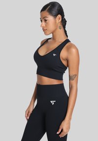 Zwarte sportbeha en high-waisted leggings van rekbare stof, met een minimalistisch wit logo op de borst en heup.