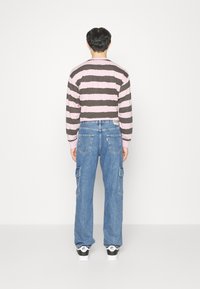 Randig långärmad topp i rosa och grått, ihop med blå cargobyxor. Outfiten har en avslappnad passform och sneakers med svarta detaljer.