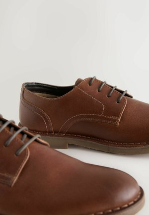 Pantofi din piele maro cu o textură netedă, vârf rotund și șireturi gri. Prezintă accente cusute și o talpă din cauciuc durabilă.