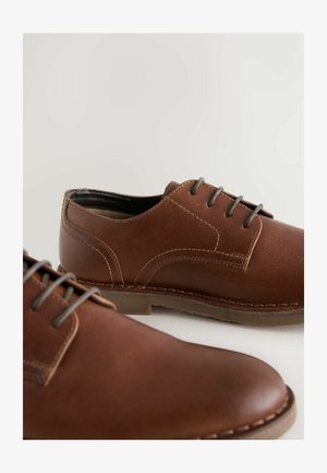 Scarpe in pelle marrone con una texture liscia, punta arrotondata e lacci grigi. Presentano dettagli cuciti e una suola in gomma durevole.