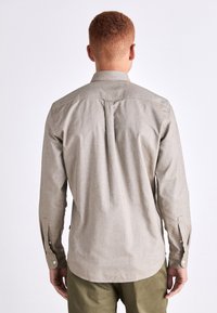 Camisa de manga larga gris claro con cuello. Presenta un plisado central, puños con botones y un dobladillo curvado. Fabricada en tela tejida.
