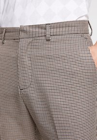 Hnědé a krémové kostkované kalhoty s rovnou přední částí, poutky na opasek a bočními kapsami; texturovaná tkanina s tkaným vzorem.