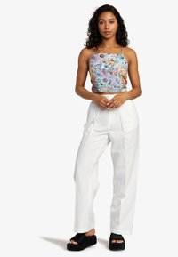 Floral crop top with colorful patterns, paired with loose white trousers and black platform sandals. Light, smooth fabric textures visible.