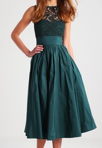 Türkises Kleid mit einem Spitzenoberteil und einem einfarbigen Taillenbund. Verfügt über einen voluminösen, plissierten Rock und ein ärmelloses Design. Strukturierte Spitzenverarbeitung am oberen Rand.