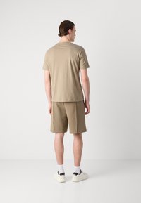 Kaki bomull t-skjorte og matchende shorts, begge med en avslappet passform. Personen har på seg hvite sokker og sneakers med svarte detaljer.