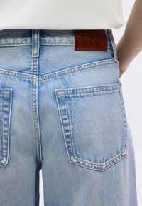 Ανοιχτό  μπλε τζιν τζιν με ψηλή μέση, ίσια γραμμή και έντονες πίσω τσέπες. Δερμάτινη ετικέτα με την επιγραφή "Calvin Klein".