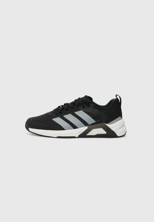 Sort atletiksneaker med tre grå striber, hvid sål og sort hælstøttedetalje, set fra siden på en lysegrå baggrund.