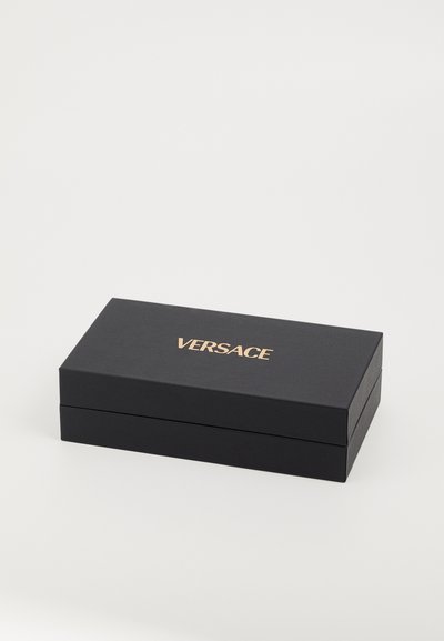 Musta ristkülikukujuline kast tekstuurse pinnaga, mille peal on kuldne "VERSACE" logo. Sulgub tasasel kaanel.