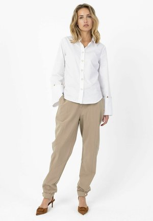 White button-up shirt with long sleeves, beige tapered pants, and brown heels. Gold button accents on shirt cuffs and pants. Smooth fabric texture.