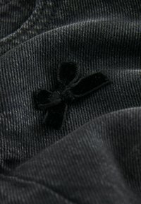 Tessuto di denim nero con una sottile trama e un dettaglio accentato da un fiocco di velluto. Il tessuto è morbido e liscio con una leggera lucentezza.