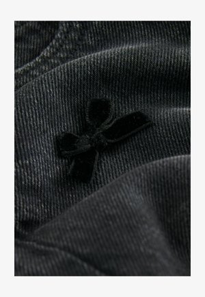 Schwarzer Denim-Stoff mit subtiler Textur und einem Akzentdetail aus Samt in Form einer Schleife. Der Stoff ist weich und glatt mit einem leichten Glanz.