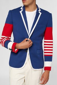 Blauwe blazer met rode accentmouwen met witte strepen. Witte revers en detail op de zak. Materiaal lijkt glad en gestructureerd.