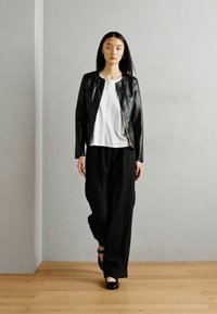 Zwarte leren jas over een witte top, gecombineerd met losse zwarte broeken. Gladde texturen en contrasterende kleuren creëren een minimalistische look.