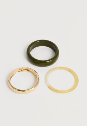 Trois anneaux lisses en vert foncé, or brillant et jaune translucide disposés sur un fond clair.