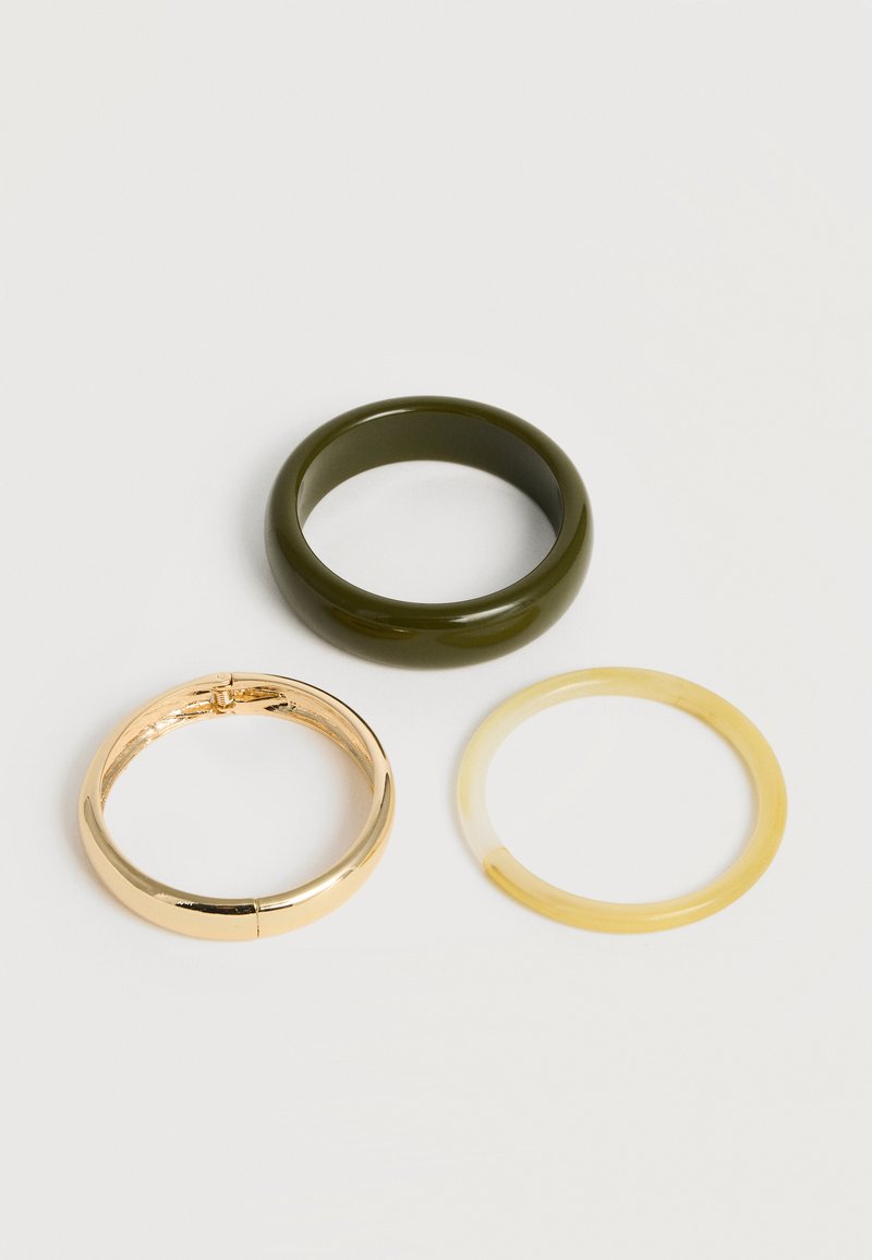 Τρεις λείες δακτυλίδια σε σκούρο πράσινο, λαμπερό χρυσό και διαφανές κίτρινο τοποθετημένα σε ανοιχτό φόντο.
