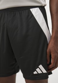 Sorte atletiske shorts lavet af glat stof med et hvidt mesh-sidestykke og et broderet hvidt Adidas-logo nederst til venstre.