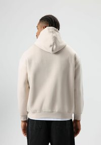 Lichtbeige hoodie met een grote, zachte capuchon, geribbelde boorden aan de mouwen en zoom. Gemaakt van soepel stof met een ontspannen pasvorm.