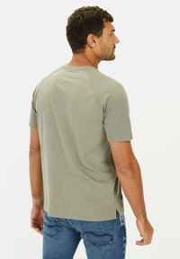 Lys olivengrøn kortærmet t-shirt med rund udskæring, søm detalje i ryggen og sideslids, parret med blå jeans.