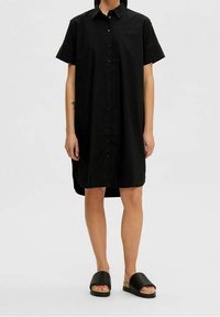 Svart skjortklänning med korta ärmar, tillverkad av ett mjukt tyg, med en rak skärning och en nederdel som sträcker sig längre bak.