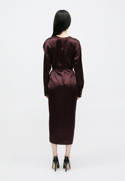 Φόρεμα μπορντό σατέν με μακριά μανίκια, εφαρμοστή μέση και μήκος μέχρι τη μέση της γάμπας. Διαθέτει απαλή υφή και μανσέτες με κουμπιά, συνδυασμένο με μαύρες γόβες.