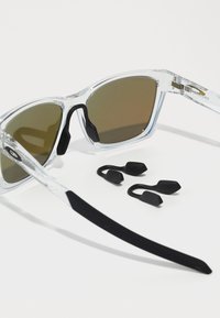 Klare Rahmen-Sonnenbrille mit braunen Gläsern, schwarzen Gummi-Nasenpads und zwei zusätzlichen schwarzen Gummi-Griffen. Gerade schwarze Bügel.