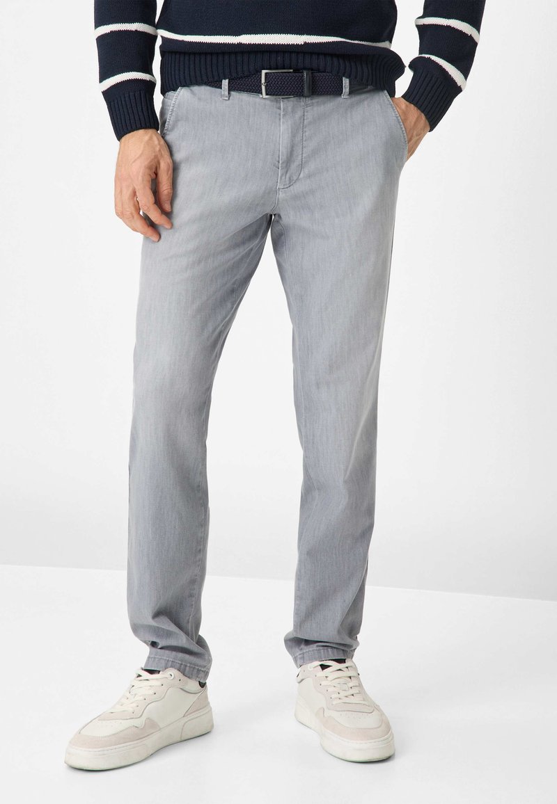 Helle graue Hose mit geradem Schnitt, aus weichem Stoff. Kombiniert mit weißen Sneakers, die eine flache Sohle und ein Schnür-Design aufweisen.