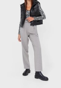 Schwarzer gepolsterter Westen über einem schwarz-weißen gestreiften Langarmshirt, kombiniert mit hellgrauen Hosen und klobigen schwarzen Stiefeletten.