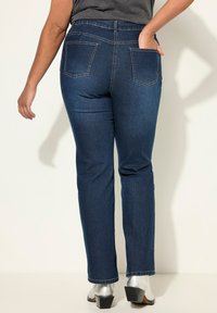 Tummansiniset farkut suoralla lahkeella, joissa on takataskut ja huomaamattomat tikkaus yksityiskohdat. Yhdistetty hopeisiin lohkokorkoihin.