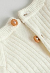 Rippenshirt in Creme mit weicher Textur, runden Ausschnitt, zwei Holzknöpfen und einem klaren, schlichten Design.