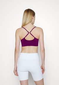 Bralette atlético roxo com alças cruzadas e uma textura suave, combinado com calções brancos de cintura alta com bolsos.