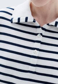Polo a righe bianche e blu navy con colletto a coste, tre bottoni e una texture morbida. Presenta righe orizzontali su tutta la superficie.
