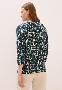 Sudadera con capucha en azul oscuro, crema y patrón abstracto en negro; mangas de tres cuartos; tejido suave; cortes laterales en el dobladillo para facilitar el movimiento.