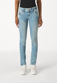 Világoskék farmernadrág, slim fit szabással, közepes derékkal, öt zsebes kivitelben és enyhe kopással. Fehér sportcipővel párosítva.