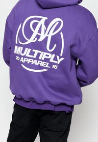 Lila Kapuzenpullover mit einem großen weißen Grafikdruck auf dem Rücken, der den Text „MULTIPLY 20 APPAREL 15“ zeigt. Gerippte Bündchen und Saum. Weicher Stoff.