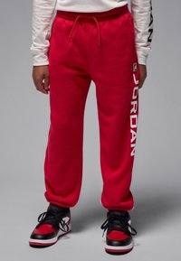 Punased dressipüksid, millel on vasakul säärel valge "JORDAN" logo, elastne vöökohal ja küljetaskud. Kandmisel musta ja punasega tossud.