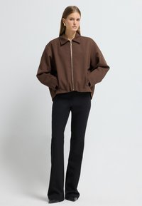 Brun cropped jakke med lynlåslukning, spredt krave og lange ærmer, parret med sorte flagrende bukser og spidse sorte sko.