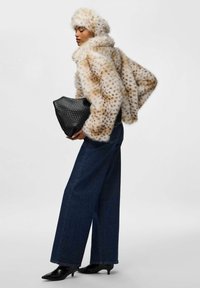 Giacca in pelliccia sintetica con motivo a macchie in tonalità crema e marrone, abbinata a jeans in denim blu a gamba larga e una borsa a tracolla nera con texture.
