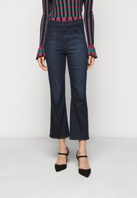Jeans de mezclilla de color azul oscuro, acampanados, con una cintura alta y dobladillo sin acabar. Combinados con un suéter ajustado de rayas multicolores y tacones negros de punta.
