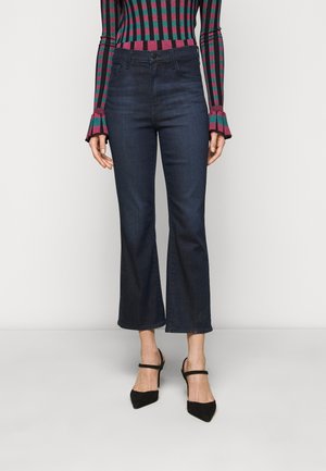 Dark blue denim flared jeans with a high waist and raw hem. Paired with a fitted, multi-colored striped sweater and black pointed heels.