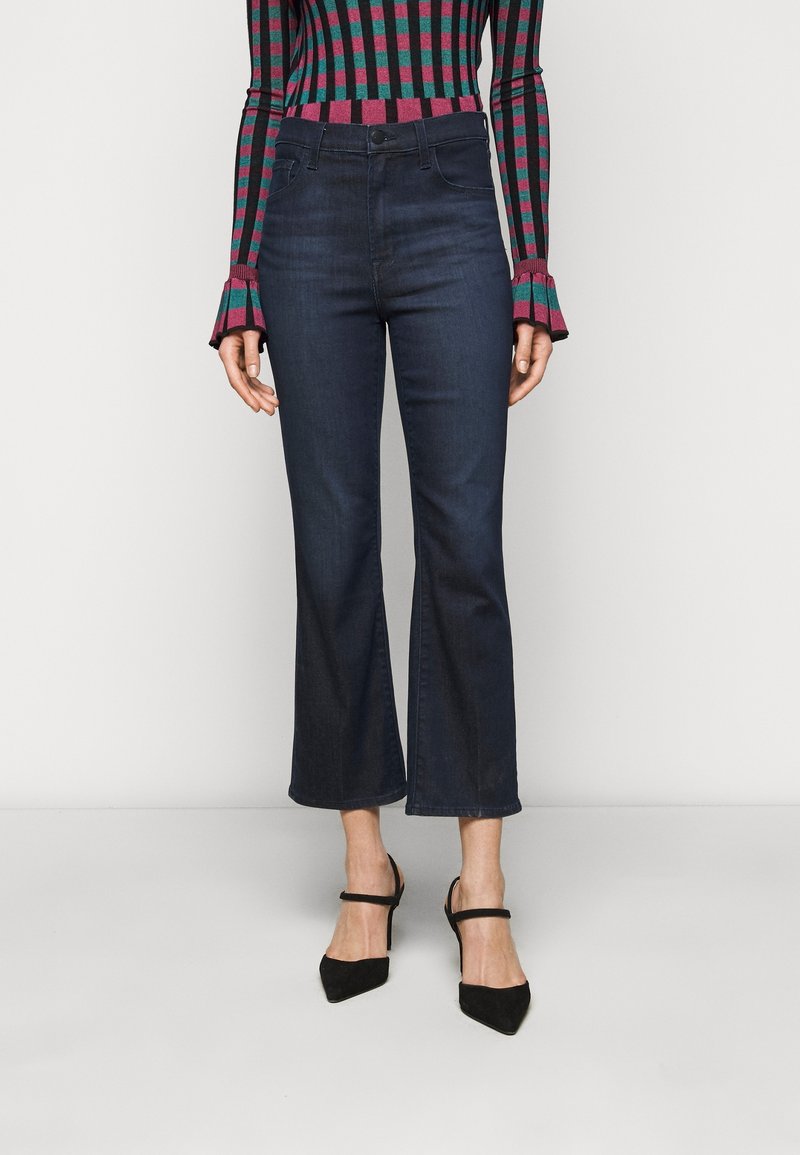 Jeans de mezclilla de color azul oscuro, acampanados, con una cintura alta y dobladillo sin acabar. Combinados con un suéter ajustado de rayas multicolores y tacones negros de punta.
