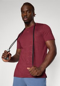 Bordeaux sportshirt met korte mouwen en een subtiel patroon, vastgehouden met een zwarte springtouw. Glad materiaal, ronde halslijn en slim fit ontwerp.