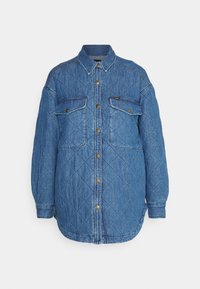 Quiltad denimskjorta i blått med knäppning, spetsig krage och två bröstfickor. Har ett texturerat diamantmönster genom hela.