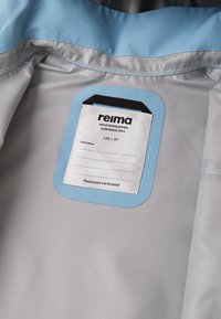 Reima vejrbestandig jakke har indvendigt et lyseblåt mærke på en grå, tekstureret foring, med en label til størrelse 128 / 8Y og brugsanvisninger.