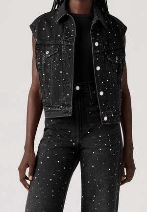 Sort ærmeløs denimjakke og matchende højtaljede jeans med spredte små sølvnitter, båret over en sort top.