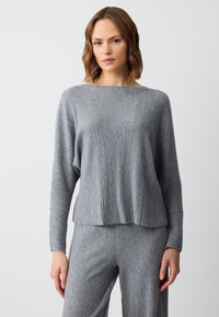 Grijze geribbelde gebreide trui met een brede bootnek en lange mouwen, met een losse pasvorm en subtiele textuur. Gecombineerd met bijpassende broek.