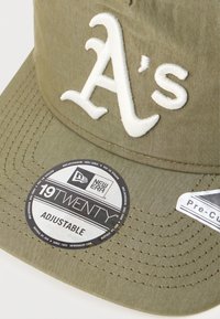 Boné ajustável verde oliva com o logótipo "A's" bordado em branco, costura em contraste e etiquetas de marca que indicam o modelo "19TWENTY" da New Era.