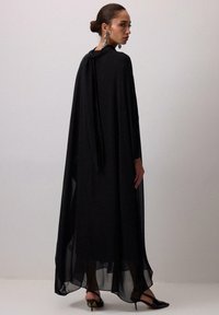 Must musta kleit, millel on sile langevus, pikad varrukad, side kaeluses ning voolav siluett. Kombineeritud mustade kontsakingadega.